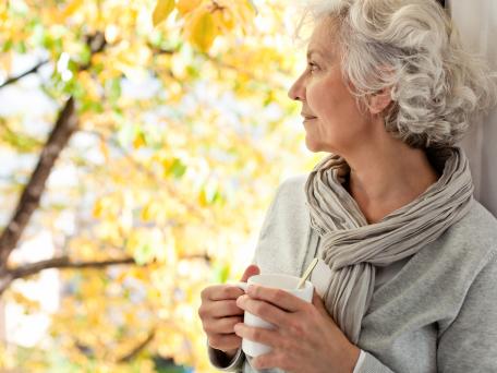 grauhaarige Frau genießt den sonnigen Herbst mit Tasse in der Hand