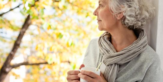 grauhaarige Frau genießt den sonnigen Herbst mit Tasse in der Hand