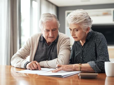 Seniorenpaar sitzt am Tisch und schaut in Dokumente