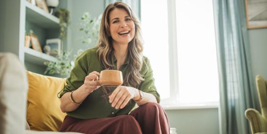 Frau mit Tasse in der Hand sitzt auf einier Couch und lächelt