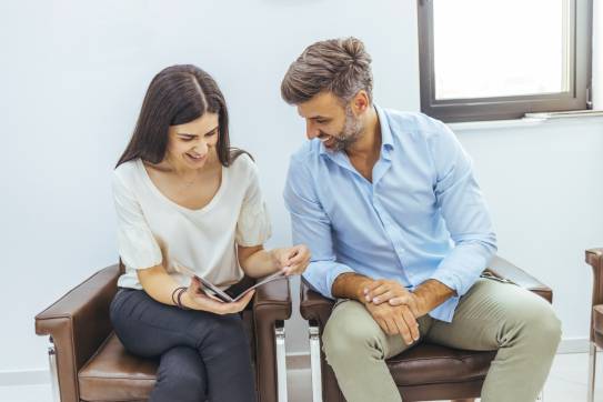 Frau und Mann sitzen im Wartezimmer und schauen in eine Zeitschrift