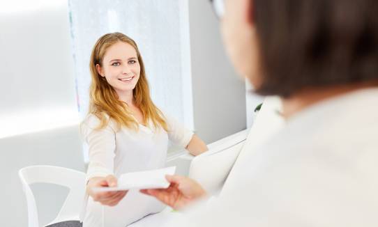 Empfangsdame überreicht Dokument an Patientin